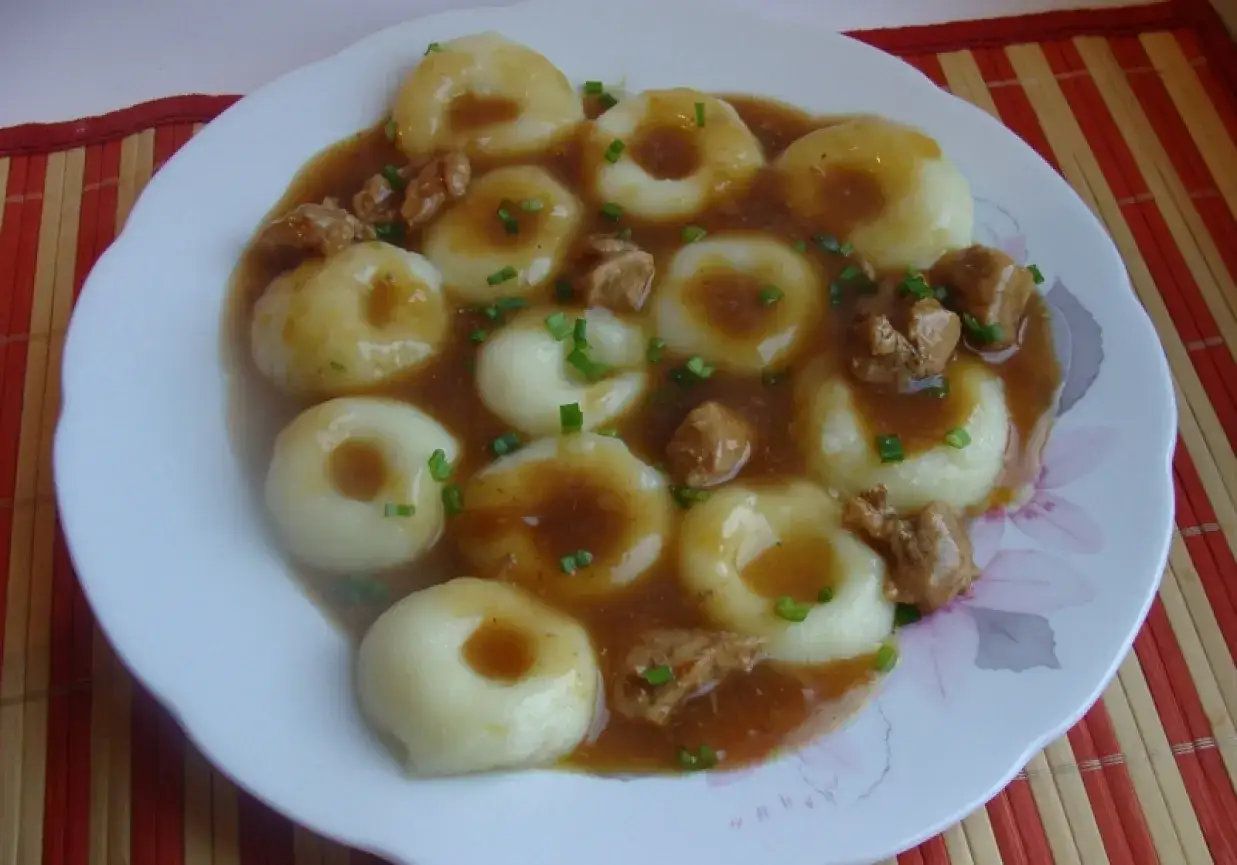 Pyszne kluski śląskie w sosie z kawałkami mięsa, posypane szczypiorkiem.