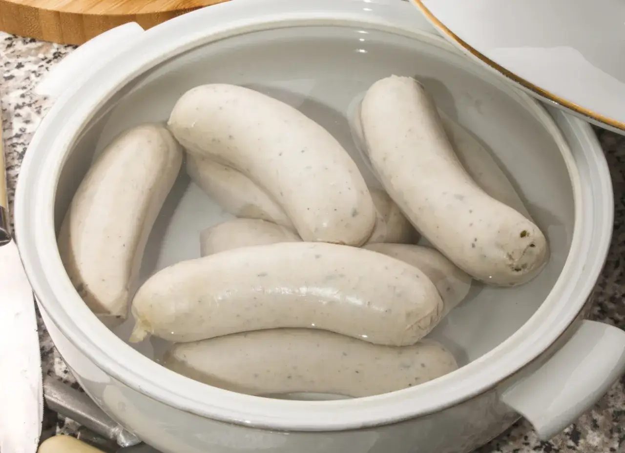 Biała kiełbasa w garnku z wodą, gotowa do parzenia. Delikatne, białe kiełbaski czekają na idealny moment, by trafić na stół.