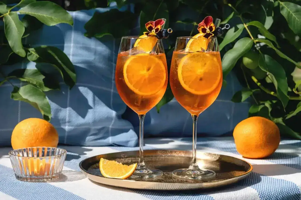 Dwa orzeźwiające drinki z aperolem i sokiem pomarańczowym, ozdobione plasterkami pomarańczy i kwiatami, gotowe na letnie popołudnie.
