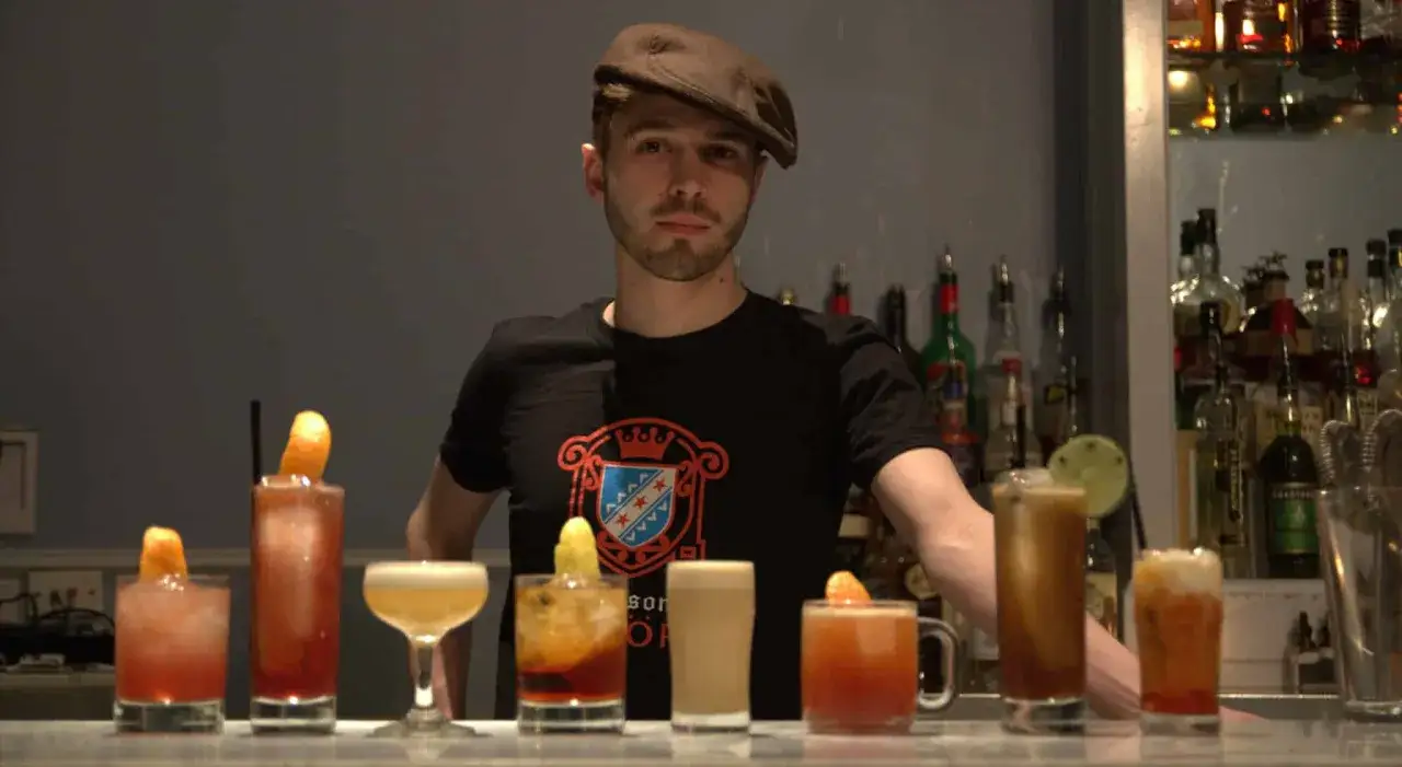 Barman prezentuje kolorowe drinki z herbatą, każdy ozdobiony owocem.