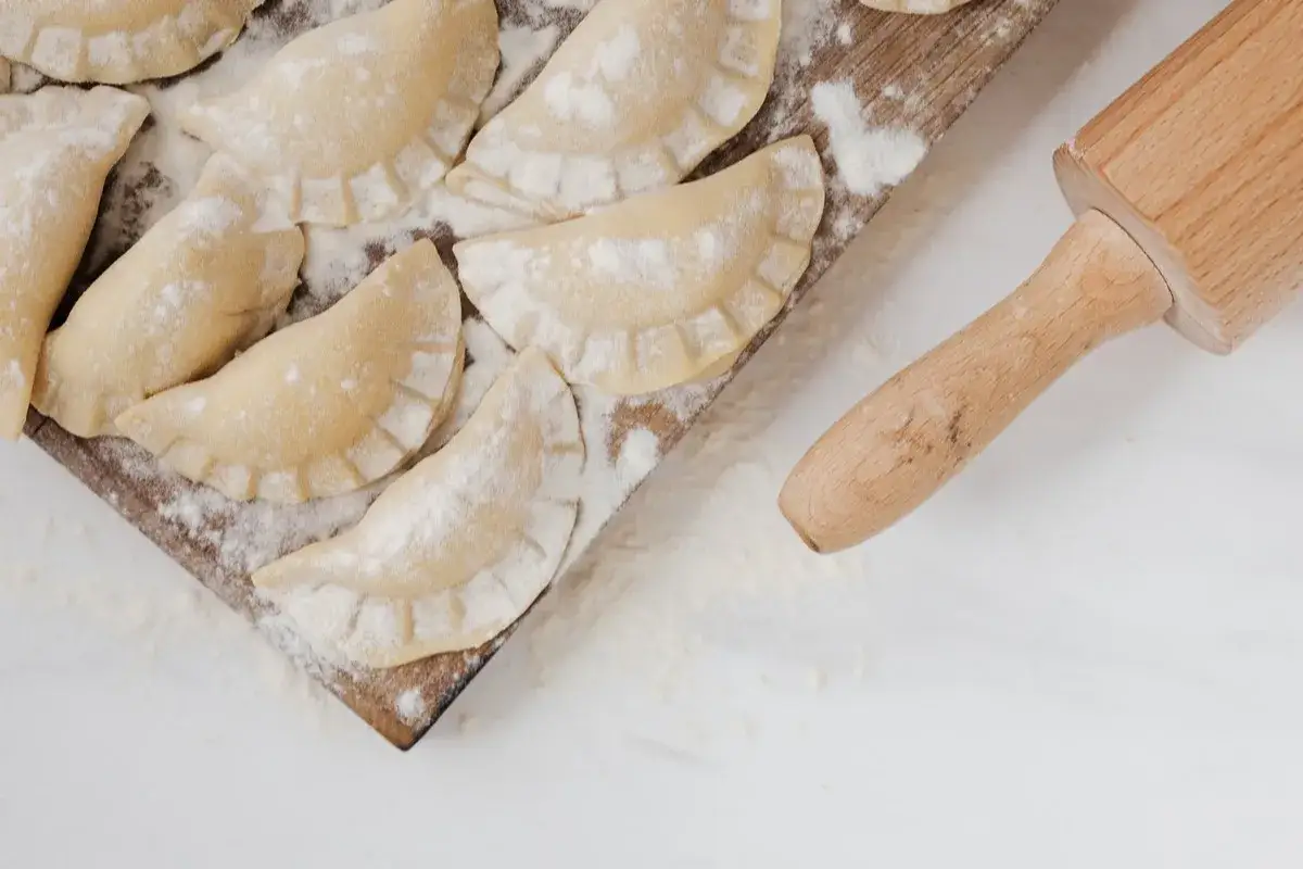 Surowe pierogi na desce, posypane mąką. Czy ciasto na pierogi można zrobić dzień wcześniej? Tak, można je przechowywać w lod&oacute;wce.