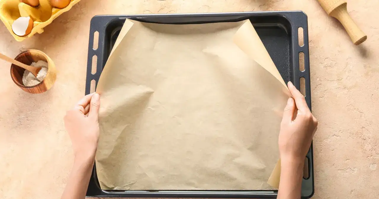 Ręce układają papier do pieczenia na blasze. To świetny sposób, by nic nie przywarło, gdy nie masz czym zastąpić papieru do pieczenia.