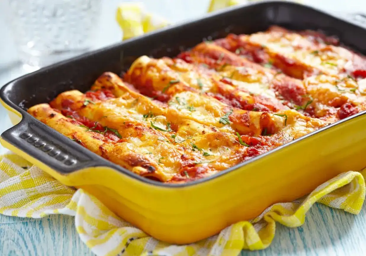 Pyszne cannelloni z mięsem mielonym, zapieczone pod sosem pomidorowym i serem, w ż&oacute;łtej naczyniu żaroodpornym.