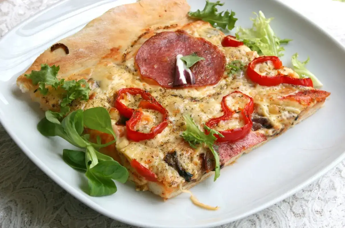 Kawałek pizzy z salami, papryką i serem na cienkim cieście na pizzę bez wyrastania, udekorowany świeżymi liśćmi sałaty.