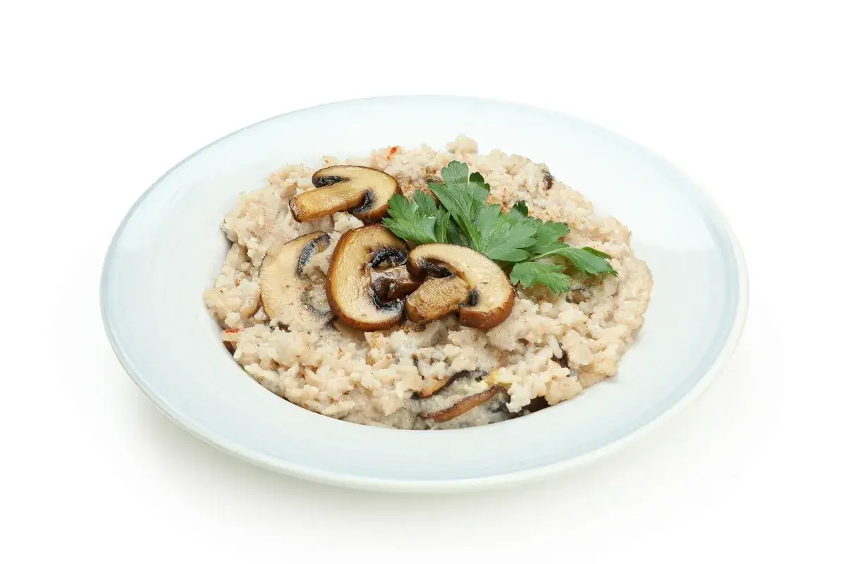 Kremowy ryż do risotto z pieczarkami i natką pietruszki na jasnym talerzu.