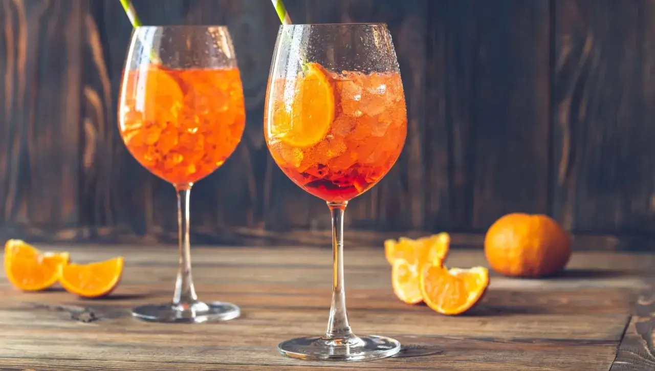 Dwa orzeźwiające drinki z aperolem, ozdobione plastrami pomarańczy, na drewnianym stole.