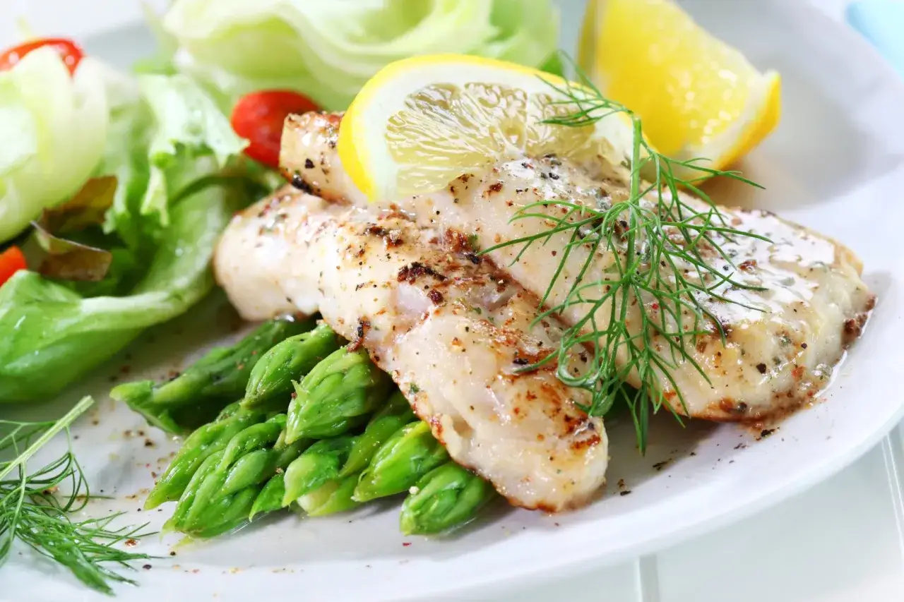 Pieczony filet rybny z szparagami, cytryną i sałatką.