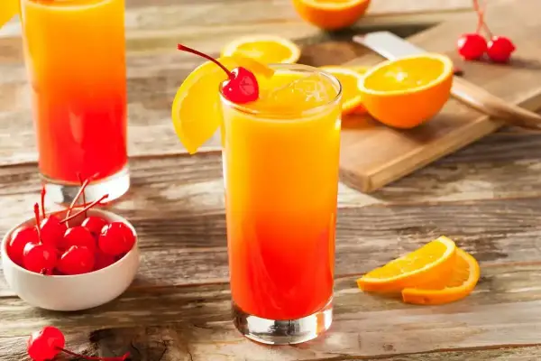 Kolorowy drink tequila sunrise z pomarańczą i wiśnią, idealny na letnie wieczory.