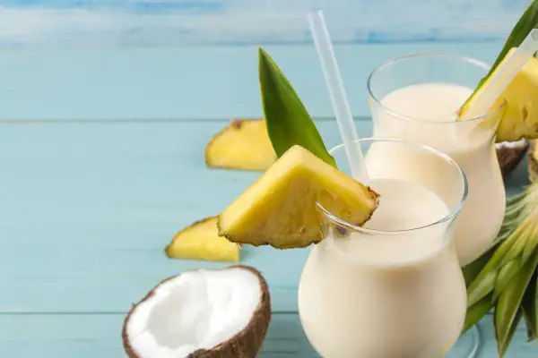 Dwa orzeźwiające koktajle pina colada z kawałkami ananasa i kokosem na niebieskim tle.