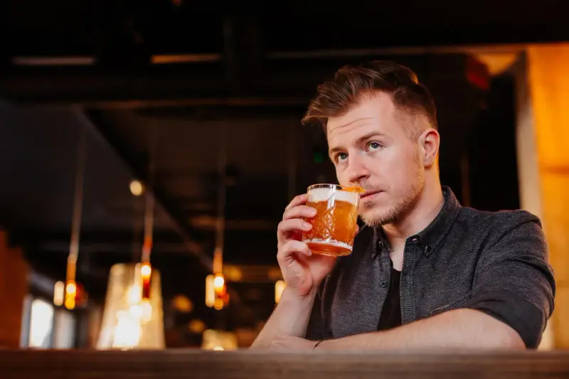 Mężczyzna sączy orzeźwiający whisky sour, delektując się smakiem w nastrojowym barze.